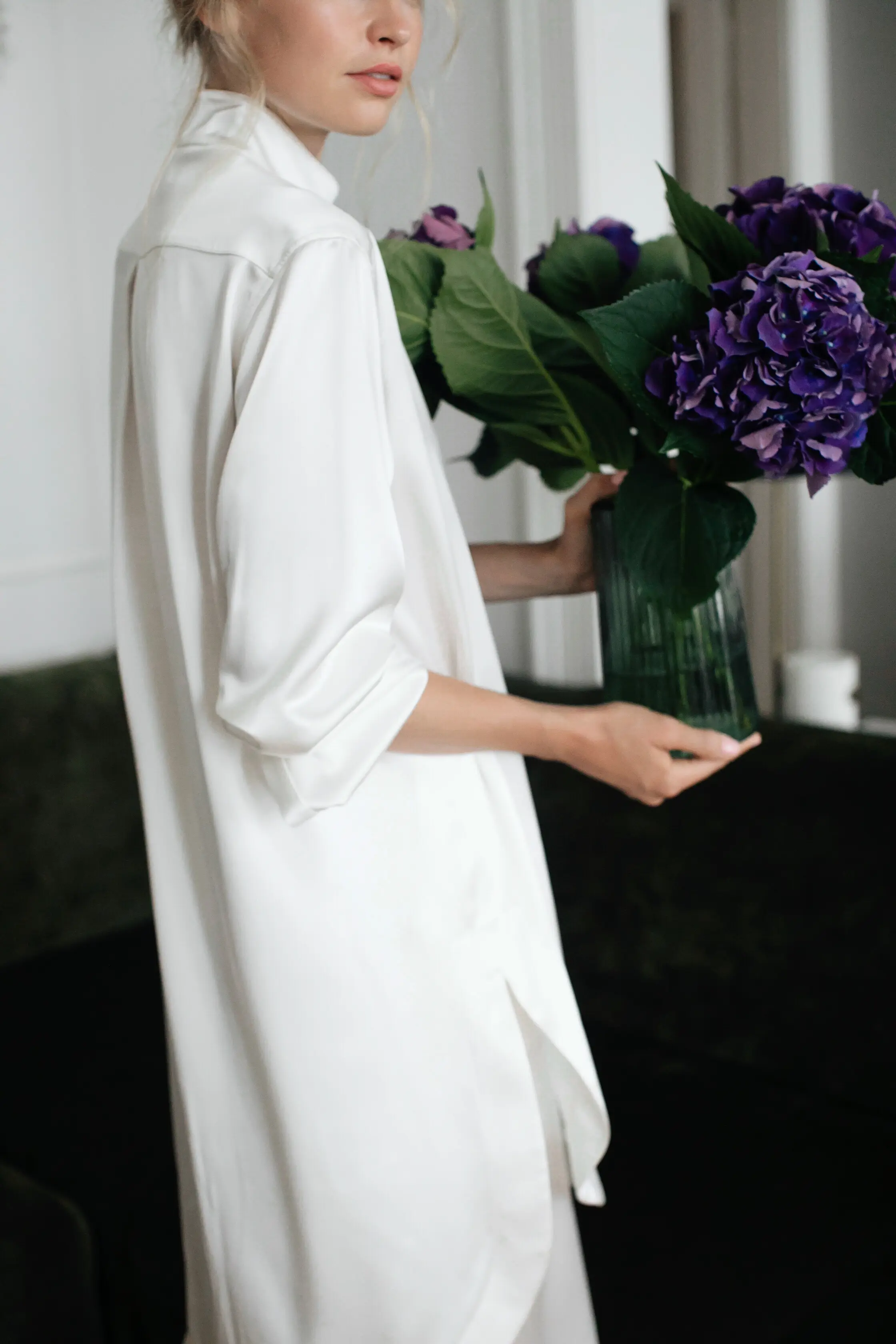 A white silk lounge shirt worn while holding a vase of hydrangeas.