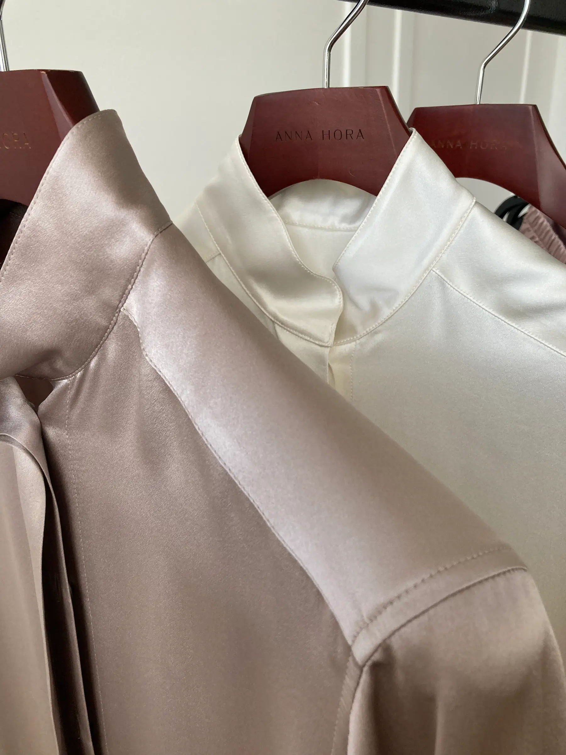 ANNA HORA silk shirts in mink and off-white hanging on branded hangers.